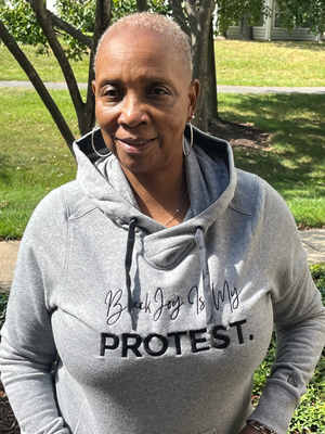 woman wearing fitted gray hoodie with black writing that says "black joy is my protest."